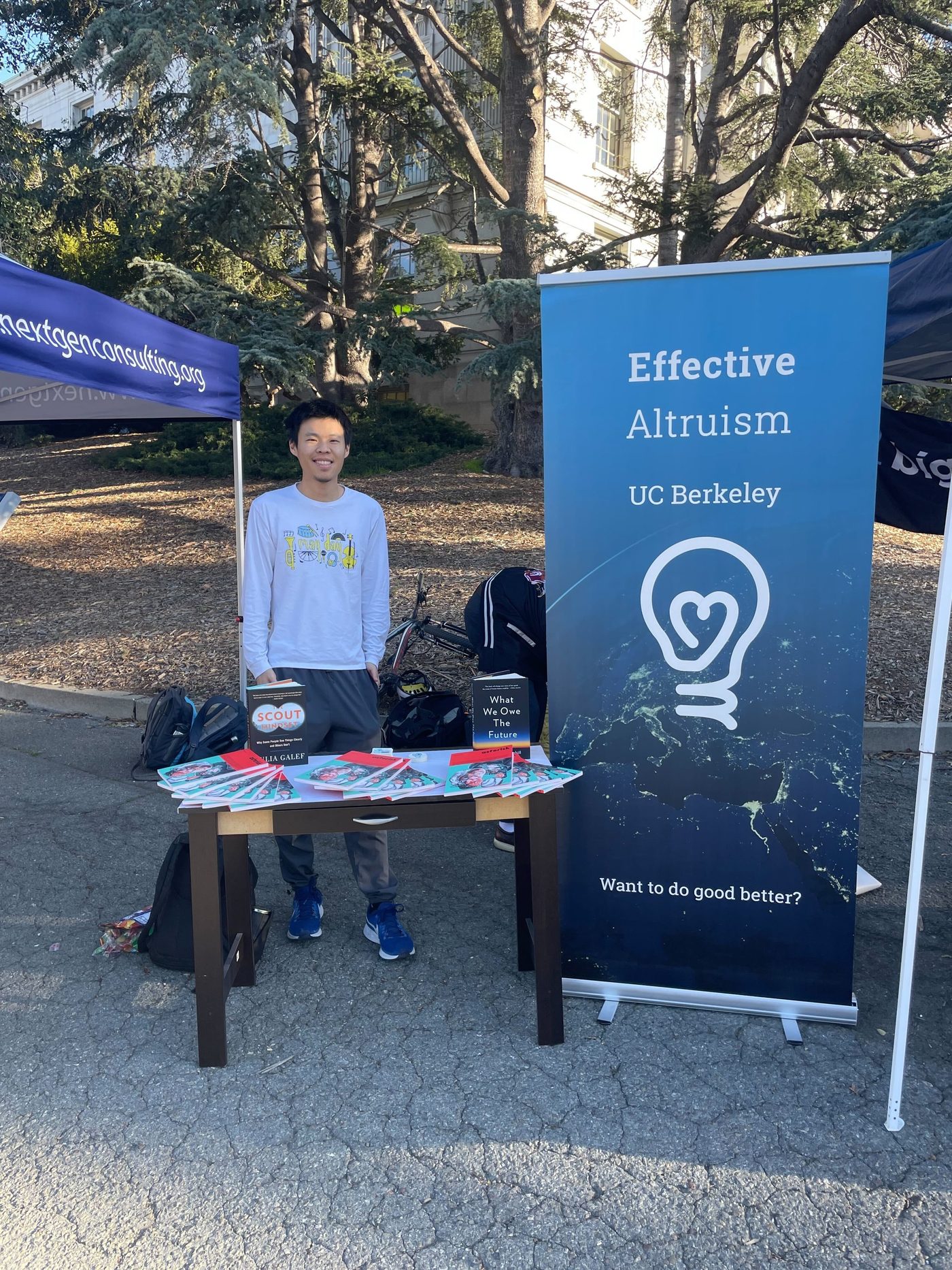 An organizer tabling for Berkeley EA on Sproul Plaza, next to a banner reading "Effective Altruism, UC Berkeley — Want to do good better?"